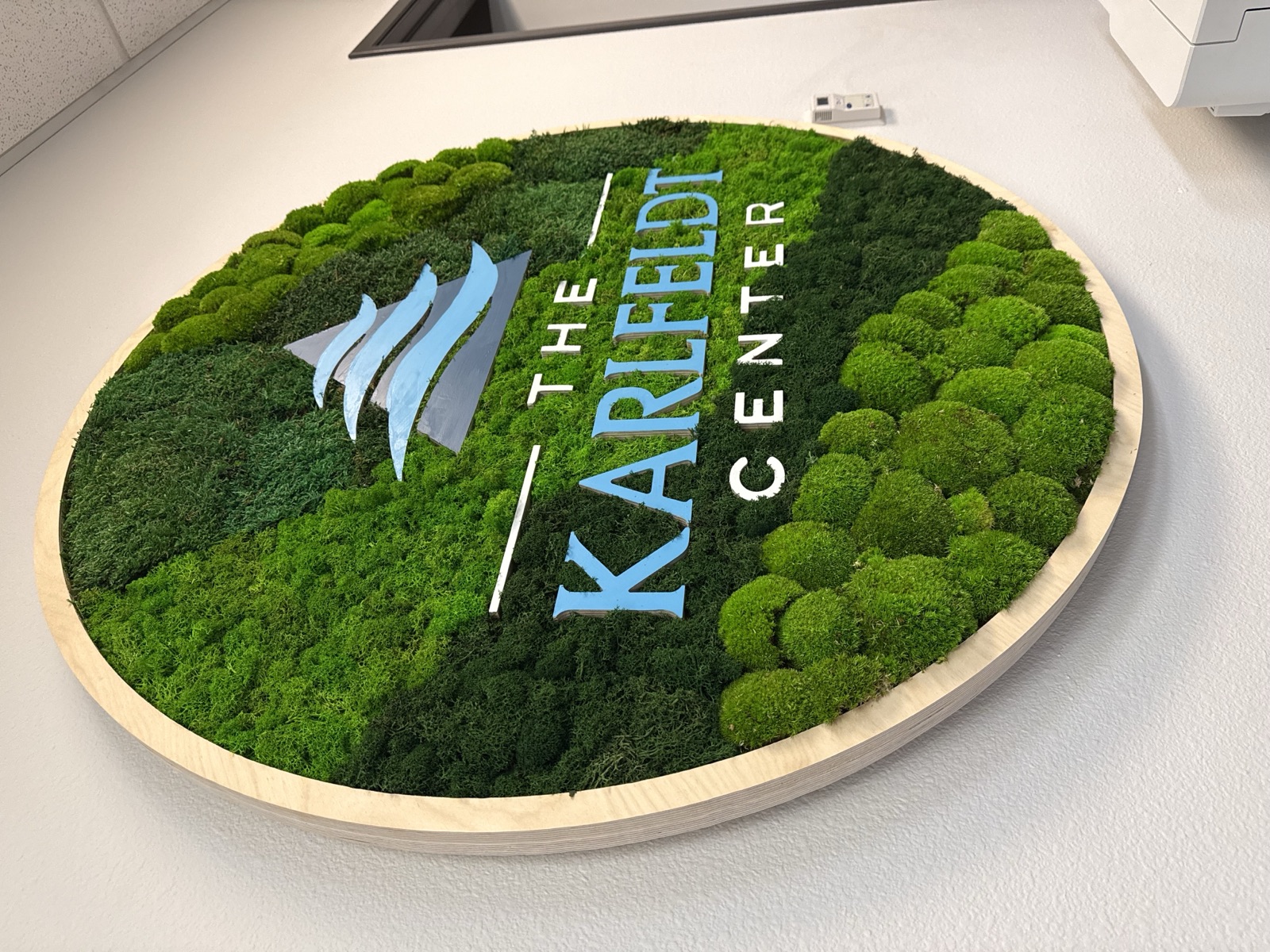 Round preserved moss sign with The Karlfeldt Center logo on a birch frame